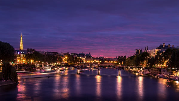 Blue hour on the Pont des Arts on the Seine and the Institut de France at Paris seen from the Pont Neuf, the old bridge of Paris. We can see, far away the Eiffel tower ("Copyright Tour Eiffel - illuminations Pierre Bideau").