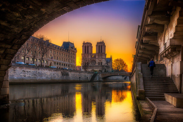 Sunrise behind the Cathedral Notre Dame de Paris and the police headquarters seen from under the Pont St-Michel, Promenade René Capitan along the Seine. We also see the Petit Pont.