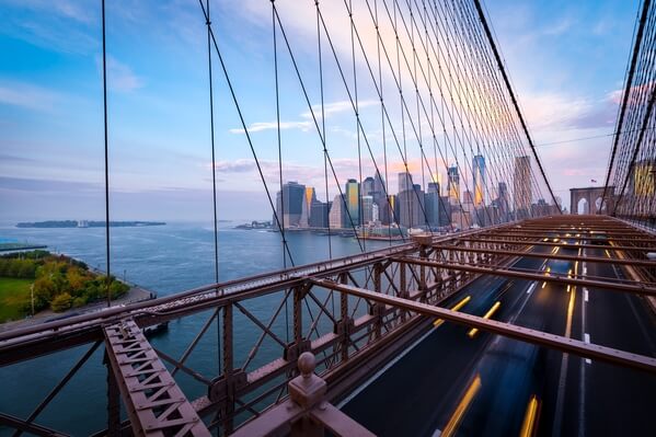 Sunset photograph of Lower Manhattan with traffic on the bridge as a blurred foreground.