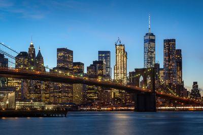 Evening shot of the Brooklyn Bridge with illuminated panorama of Lower Manhattan in the background.