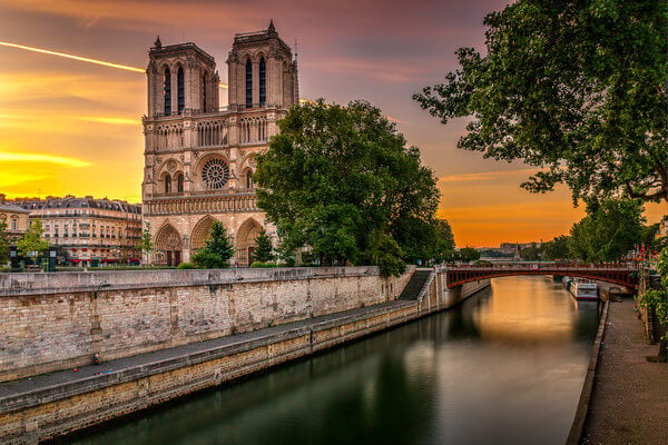 Sunrise on the Cathedral Notre Dame of Paris seen from the Petit Pont with in the foreground, the Seine and the Promenade Maurice-Carême. In the background, we can see the bridge the Pont de l’Archevéché.