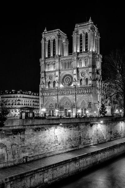 Cathedral Notre Dame of Paris seen from the Petit Pont during the the night in B/W. In the foreground, we can see the Seine and the Promenade Maurice-Carême