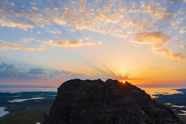 A lone hiker watches the sunset from the western peak of Stac Pollaidh