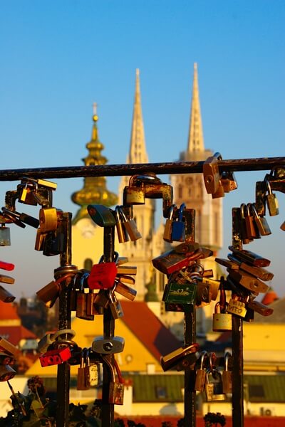 Sunny winter afternoon on Strossmayer promenade: fence with locks on east end with view on three towers of cathedral and Virgin Mary church
