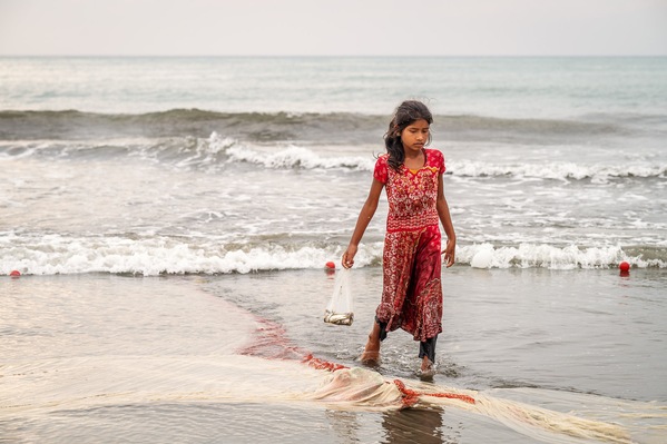 Young girl collecting left over fish on the beach
