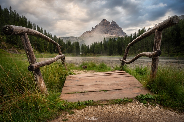 The Tre Cime peaks viewed through the Lago Antorno wood bridge, right after a rainy night