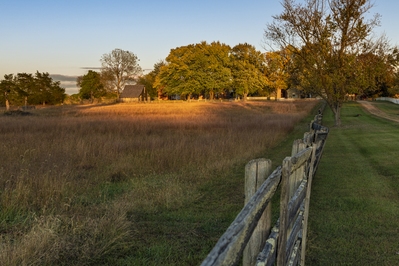 Meeks stable from the west side of the Richmond-Lynchburg Stage Lane. The sun sets behind the hill to the west and various parts of the village are separately illuminated at sunset.
