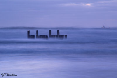 Long exposure of sea surrounding timbers that are visible at a lower tide