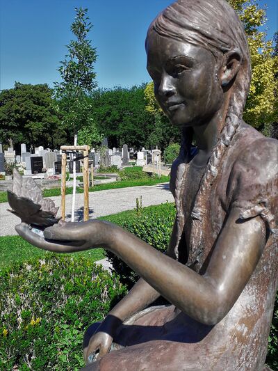 Portrait of a statue of a young girl holding a butterfly in her hand. At the 'head' of a young child's grave..