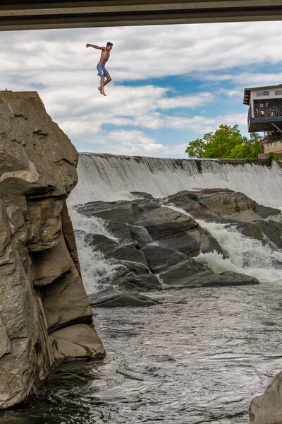 Young man jumping from the rocks beneath the bridge.