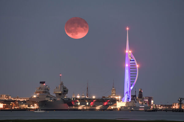 Full moon over Portsmouth skyline with HMS Queen Elizabeth aircraft carrier.