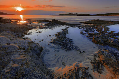 Shot over the beach with rock pools in the forground, sunset